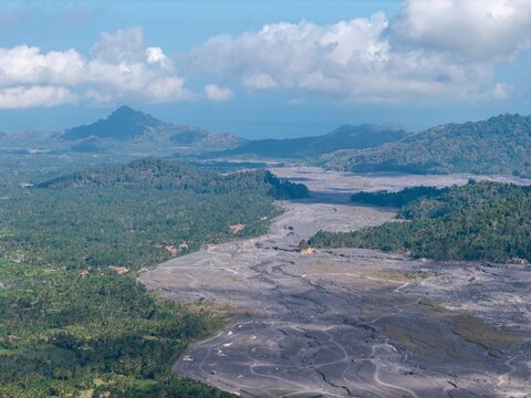 Aerial view of volcanic lahar channel cutting through tropical forest, coconut plantations, villages, and roads near Lumajang.