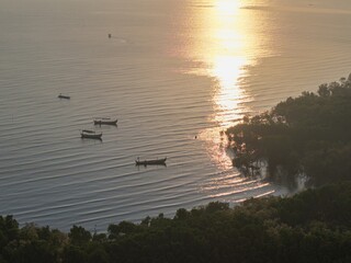 Golden sun dips low over calm waters. Small boats drift gently on serene lake surface at Probolinggo © Cloudyew