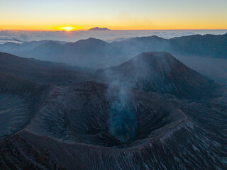 Misty volcano Mount Bromo breathes smoke into dawn soft glow. Sun rises behind distant peaks © Cloudyew