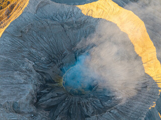 Volcano Bromo erupts, releasing mist and smoke. Rugged crater walls show deep, jagged textures © Cloudyew