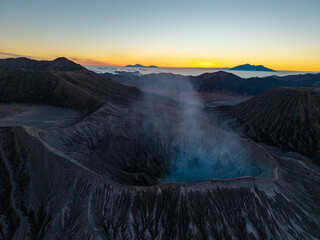 Volcanic Bromo crater glows with mist and blue lake. Sunset paints sky in warm amber hues © Cloudyew