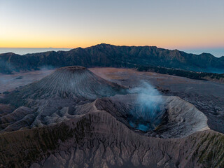 Aerial drone view of Mount Bromo volcanic caldera and rugged ridges glowing beneath a warm sunset sky. © Cloudyew