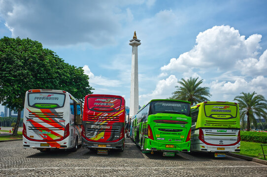 Indonesia, Jakarta &ndash; December 12, 2025: Colorful tour buses lined up in front of Monas tower with palm trees and greenery under a bright partly cloudy sky