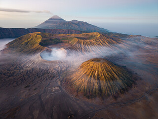 Volcanic Mount Batok peaks rise above misty, rugged terrain. Soft dawn light bathes the landscape in warm hues © Cloudyew