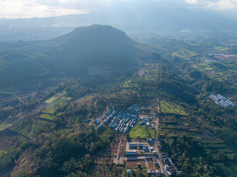 Sunlight glints through misty mountain peaks. Villages nestle in valley embrace at rural Malang
