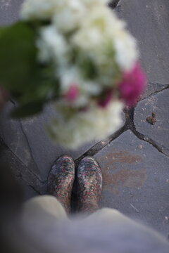 Top view on woman legs in grey rubber boots holding beautiful blurred flowers. after rain. white and pink flowers in bouquet. Girl choosing flowers on the street market. Stock Photo