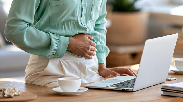 Woman experiencing abdominal discomfort while working remotely at a laptop, one hand on stomach, digestive pain, gastritis, menstrual cramps, workplace health, sick leave concept,