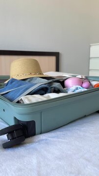 Packing a suitcase with summer clothing, a straw hat, and accessories on a bed, showcasing a minimalist approach to travel essentials and conscious consumption