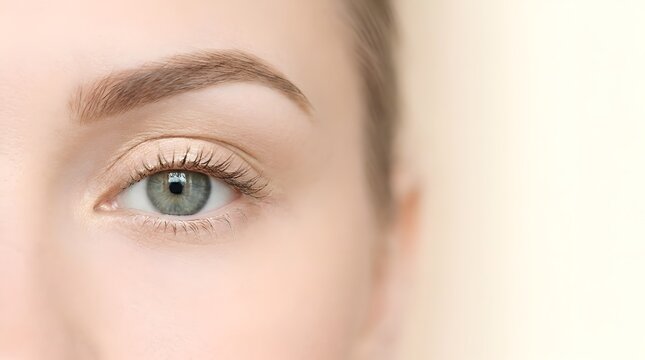 Macro shot of a detailed human eye with a shimmering green iris and subtle gold eyeshadow, showcasing long defined lashes and a perfectly shaped brow in a bright and soft lighting.