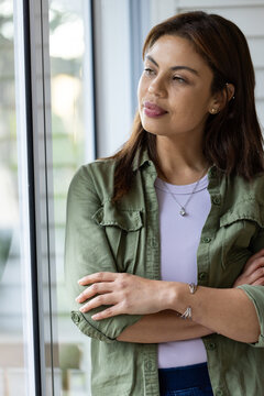 African American woman standing arms crossed in room gazing out glass window in olive shirt pendant