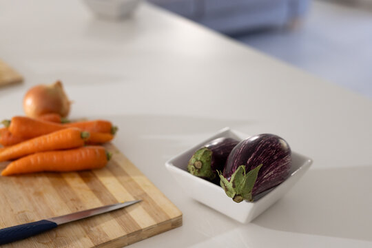 Two purple white striped eggplants sitting in white square bowl on countertop, with cutting board