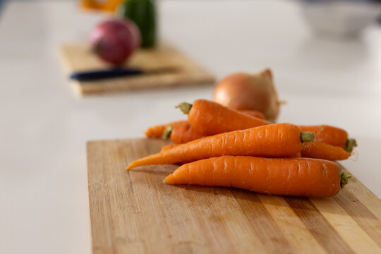 Bright orange carrots are resting on wooden cutting board on white countertop, with onion