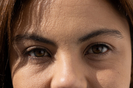 Adult female holding gaze toward camera in tight closeup, sunlight highlighting eyes and skin