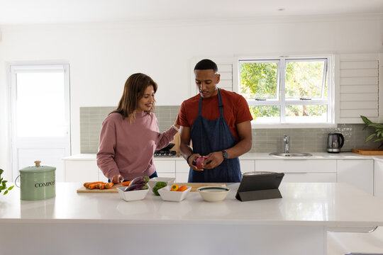 African American couple, man in red apron, chopping vegetables on island using tablet and compost