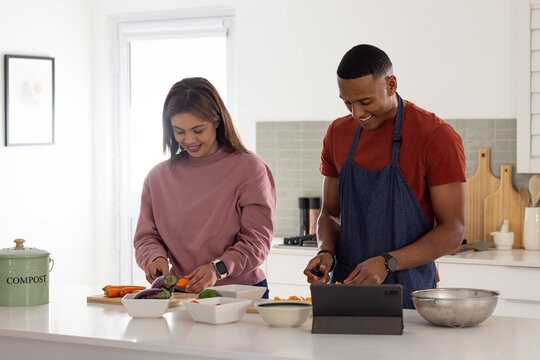 African American couple chopping vegetables at kitchen island, using tablet, prep bowls