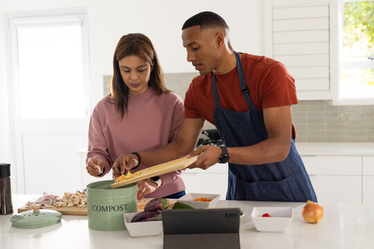 African American couple in denim apron preparing food, sorting scraps into COMPOST bin on island