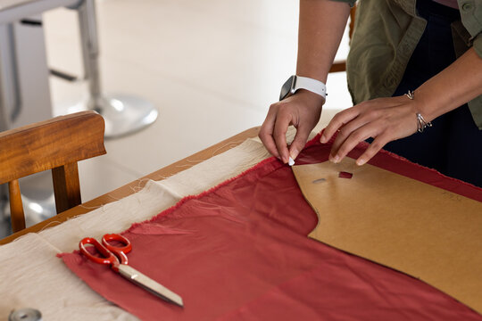 African American female smoothing cardboard pattern on red fabric at craft table