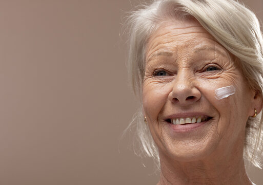 Senior woman smiling in portrait studio, showing facial cream dab and gold hoop earring