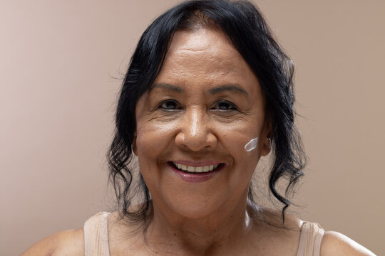 Senior African American woman smiling, showing cream dab on right cheek wearing tank top in studio