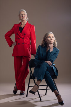 Mature female models posing in studio wearing red teal suits with black folding chair and heels