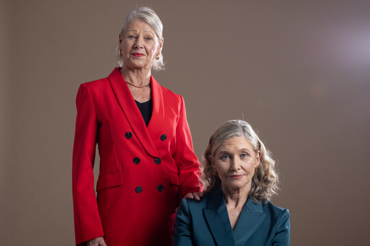 Senior female friends posing together in portrait studio wearing red and teal blazers