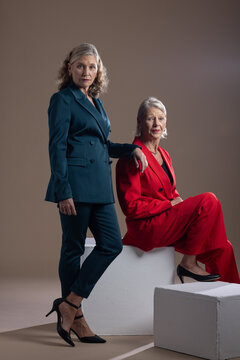 Female colleagues posing in studio on beige backdrop using white plinths with tailored suits