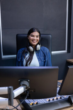 African American woman sitting behind mixing console in studio wearing denim jacket and headphones