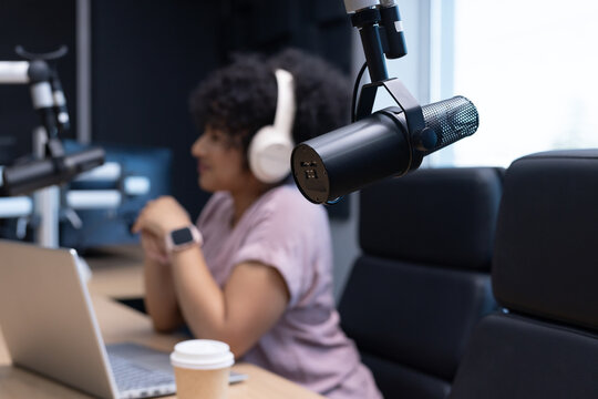 African American woman wearing purple tee, headphones, recording podcast in studio with boom mic