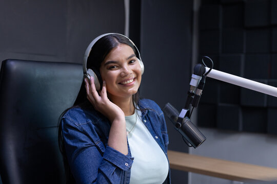 African woman recording in studio wearing denim jacket and headphones while talking into microphone