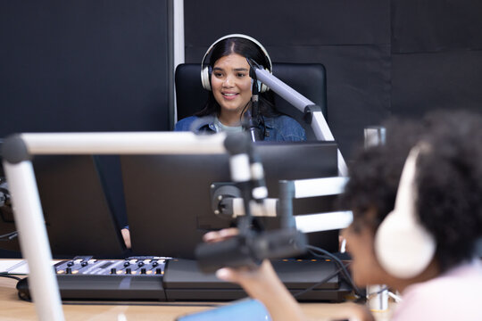 African American women recording show in studio wearing denim jacket, white headphones and boom mic