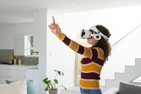 Teenage female wearing striped sweater using VR headset reaching forward in modern home, copy space