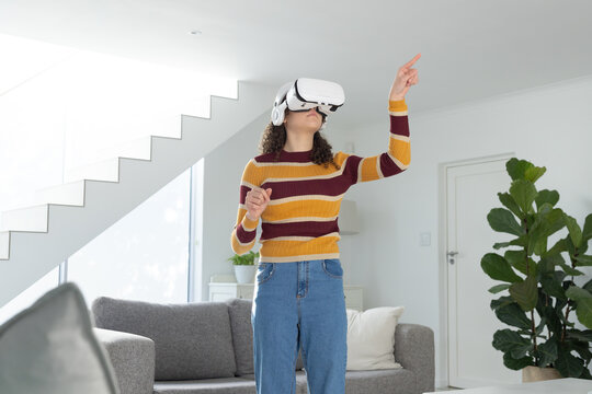 Teenage African American female in striped sweater and jeans using virtual reality headset at home
