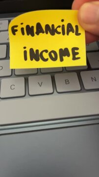 Hand holding financial income sticky note over laptop keyboard