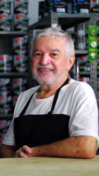 Warm portrait of smiling senior craftsman leaning on store counter wearing work apron for authentic retail customer service, lifelong trade experience, and trusted community care
