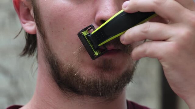 Man trims his beard with an electric trimmer in a bathroom setting