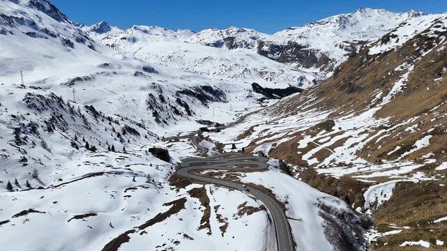 winding mountain road descends through snowbound valley single car navigates switchback bends julier pass crossing graubunden switzerland high altitude alpine route panorama