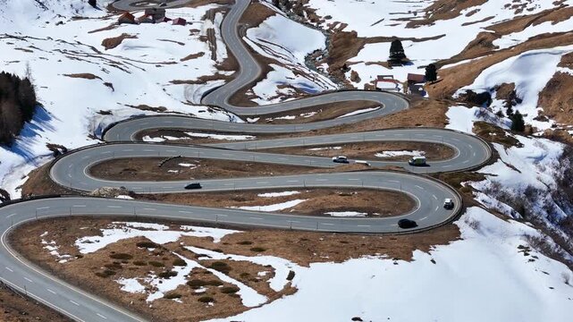 convoy of cars winds through switchback complex past roadside huts dry slopes snow patches julier pass mountain crossing graubunden switzerland high altitude alpine route