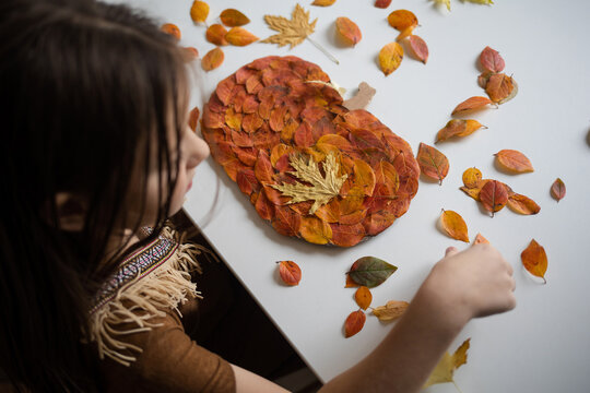 craft for kids. DIY autumn craft from leaves - pumpkin for thanksgiving day. create art for children. girl at home at the table.