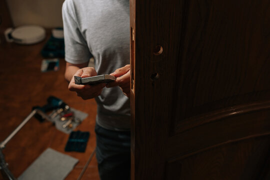 Close-up cropped shot of handyman installing door lock mechanism into door frame, performing essential repair and maintenance, enhancing home security, functionality during home improvement project.