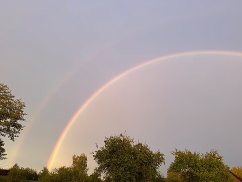 Brilliant double rainbow arching over green trees in rural landscape
