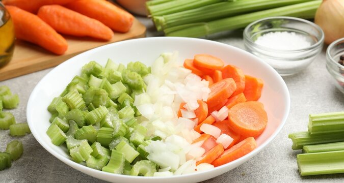 Cut carrots, onions and celery on grey table, closeup