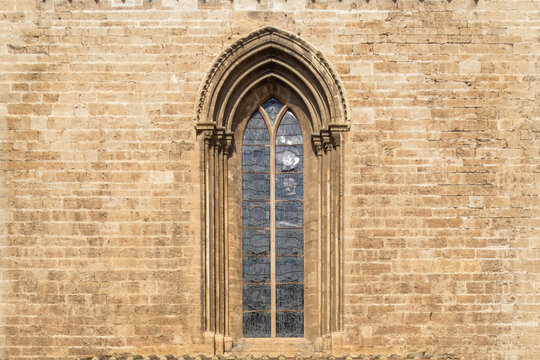Valencia Cathedral exterior showcasing a tall ogival window featuring intricate stained glass panels and multiple pointed concentric arches carved into the ancient stone wall