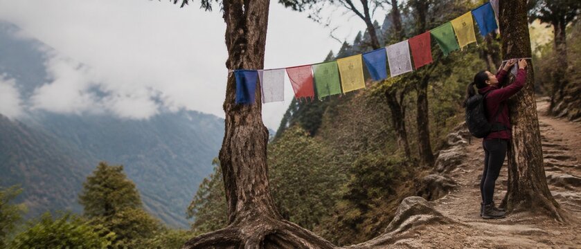 Woman hanging prayer flags on a tree in a mountainous landscape
