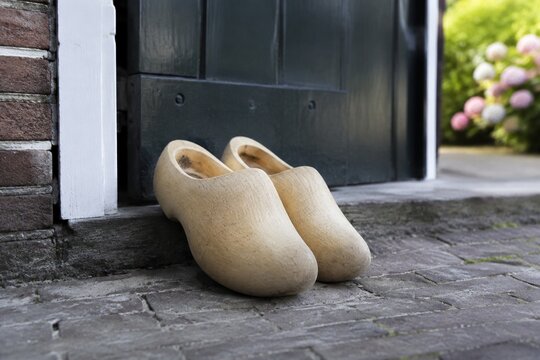 Pair of traditional light wooden Dutch clogs by a dark green door