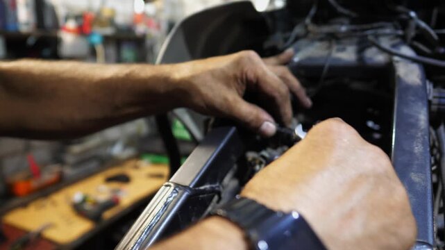 Male hands of repairer fixing moto engine at workshop. Arms of professional mechanic repairing detail of motorcycle at workplace. Adult repairman mending vehicle motor at garage. Maintenance service