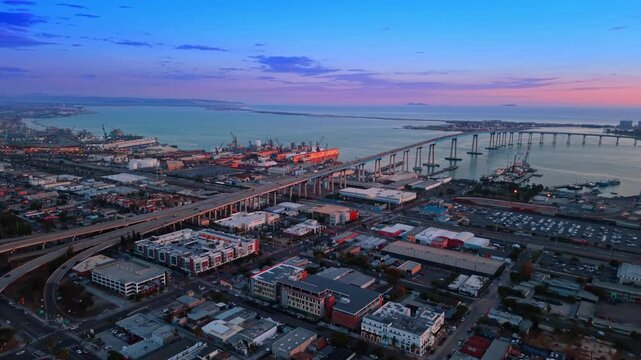 Moving over the cityscape to approach the Coronado Bridge in San Diego, California, USA. Beautiful pink sky over the waterscape in the backdrop.