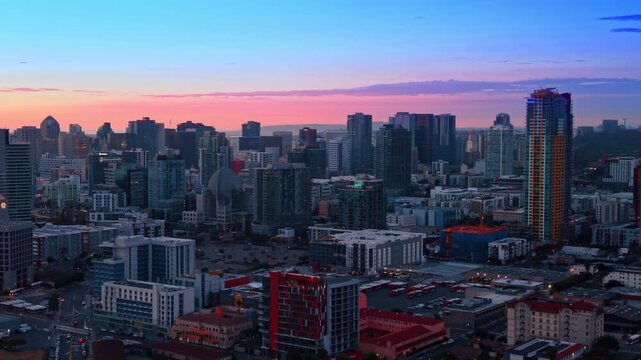 Going up over the scenery of San Diego, California, USA at dusk time. Grey high-rises of the city against pink blue-sky.
