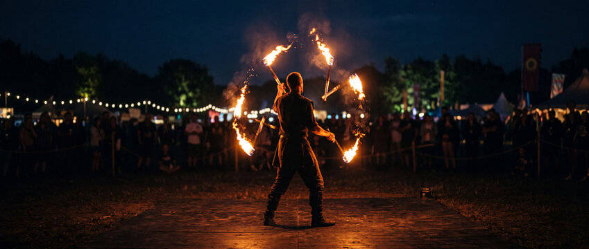 Fire performer spinning flaming torches at night festival performance with crowded outdoor audience