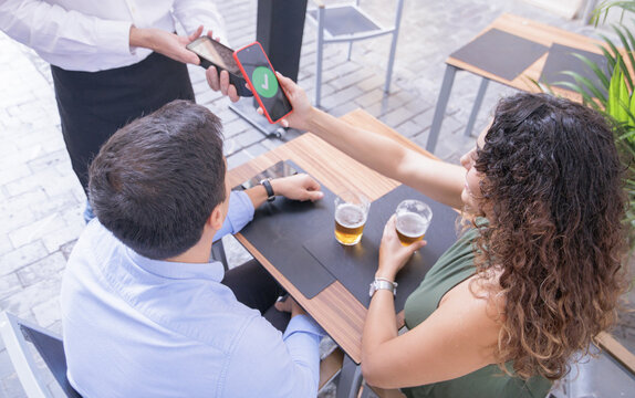 A couple paying with their cell phones for the beers they've had at a bar