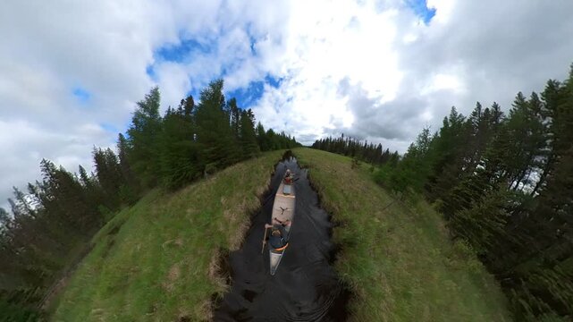 Extreme angle globe like view of two people paddling a canoe along a narrow park stream
